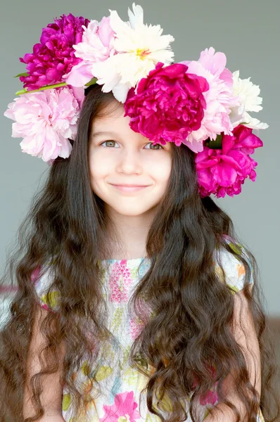 Entzückendes kleines Mädchen mit Kranz aus Pfingstrosenblumen im Atelier Stockbild