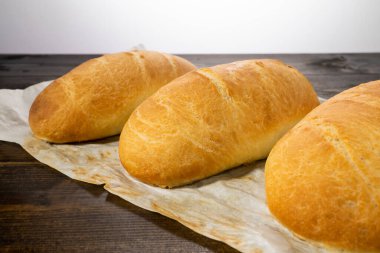 Koyu ahşap bir masanın üzerinde taze ekmek somunları yatıyor.
