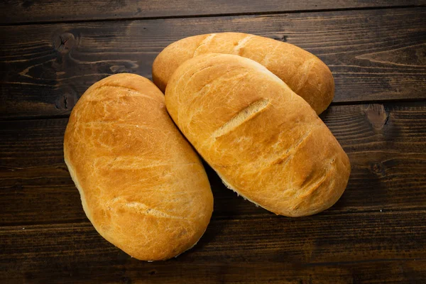 Koyu ahşap bir masanın üzerinde taze ekmek somunları yatıyor.