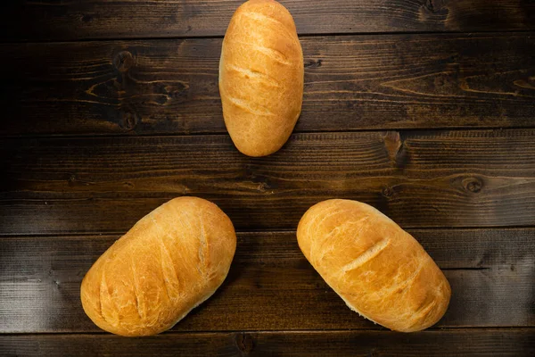 Koyu ahşap bir masanın üzerinde taze ekmek somunları yatıyor.