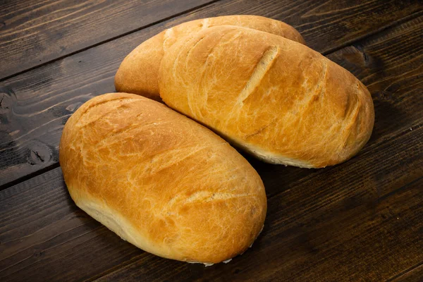 Koyu ahşap bir masanın üzerinde taze ekmek somunları yatıyor.