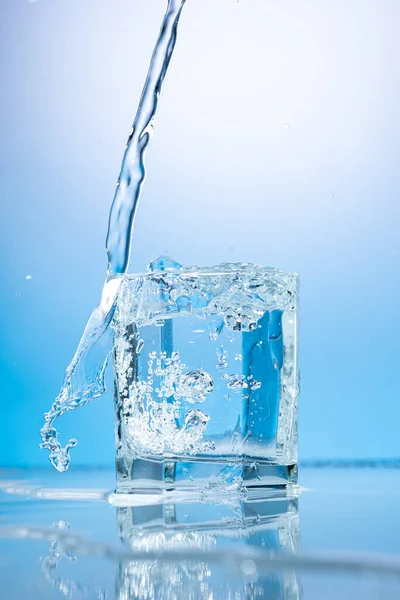 青い背景の透明なガラスの中に水を撒き散らし — ストック写真