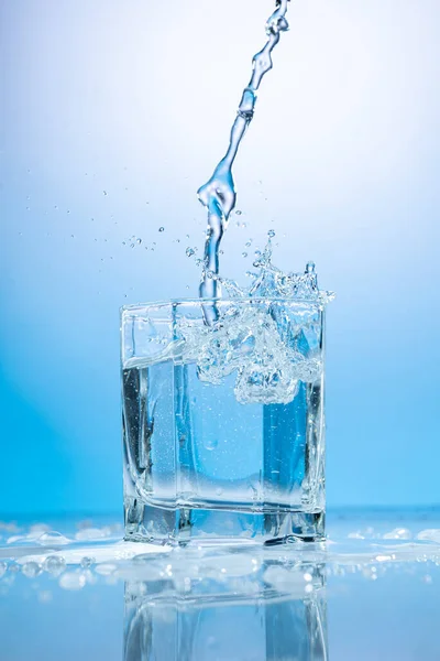 Stänk Vatten Ett Transparent Glas Blå Bakgrund — Stockfoto