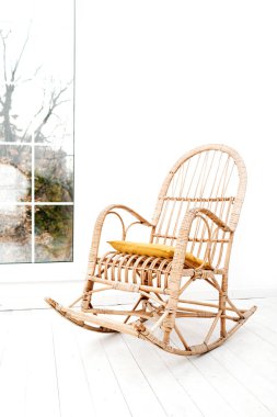 Beyaz minimalist oturma odası. İçi rattan koltuklu ve yere geniş pencereli. Çağdaş ve otantik ev dekoru kavramı. Oturma odasında sallanan hasır sandalye..