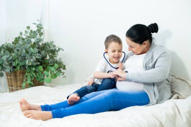 Hamile bir kadın en büyük oğluna bebeğin kalp atışlarını dinlemesi için verir. Konsept: annelik, dost canlısı aile. Ağabey!