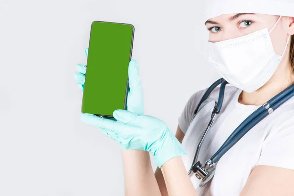 Doktor. Steril maskeli ve eldivenli bir kadın elinde bir hromokey ile telefonu tutuyor.