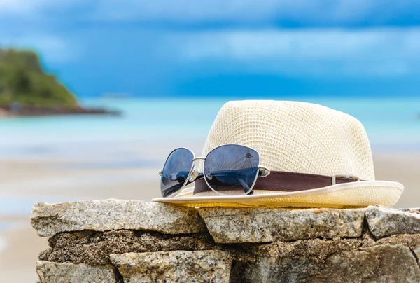 Chapéu e óculos na parede de pedra com fundo de praia — Fotografia de Stock