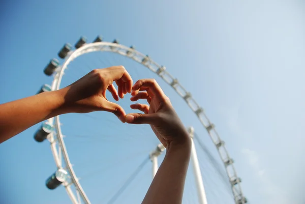 Human hand forming a love symbol with furish wheel background — Stock Photo, Image