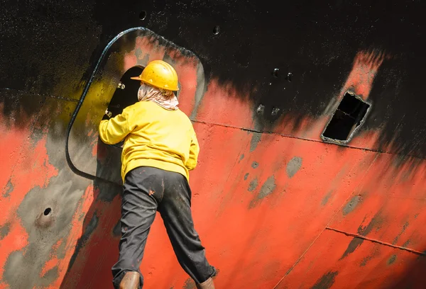 Worker cleaning side of ship at shipyard — Stock Photo, Image