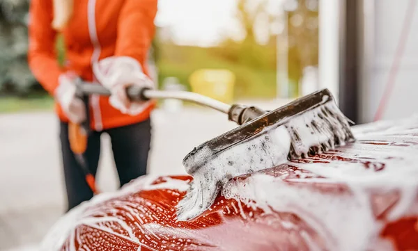 Egy fiatal nő önkiszolgáló autómosóban takarít. Szoros részlet a fehér szappan hab és ecset mozog a tető — Stock Fotó