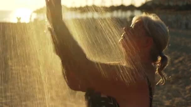 흰머리를 나이든 할머니가 아침에 해변에서 샤워를 얼굴을 햇빛을 배경으로 빛난다 — 비디오