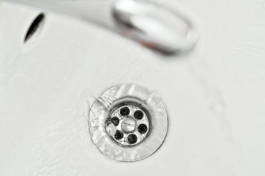 Musluktan aşağı akan su, yukarıdan görünen, gümüş musluk deliğindeki detay.