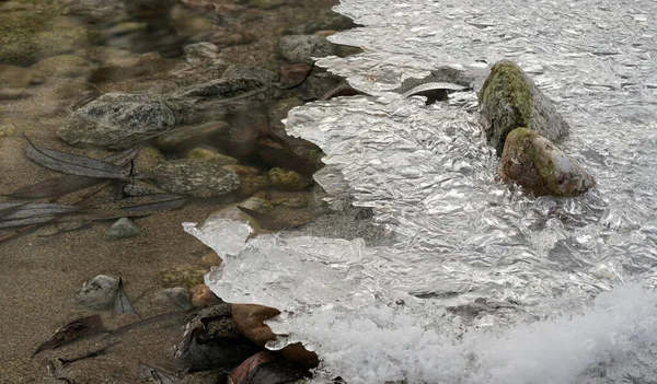 Thin ice covering rocky river shore, water flowing near - closeup winter detail — Fotografia de Stock