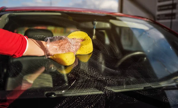 Jovem mulher limpando para-brisa de seu carro, close-up detalhe na mão em luva segurando esponja amarela — Fotografia de Stock