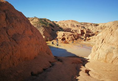 Ilakaka, Madagascar - April 30, 2019: Group of unknown Malagasy men mining sapphire in surface lake mine with shovels on a sunny day, dry red ground hills around