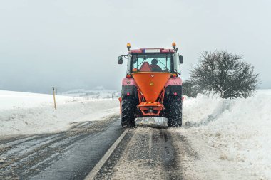 Small gritter maintenance tractor spreading de icing salt on asphalt road, view from car driving behind