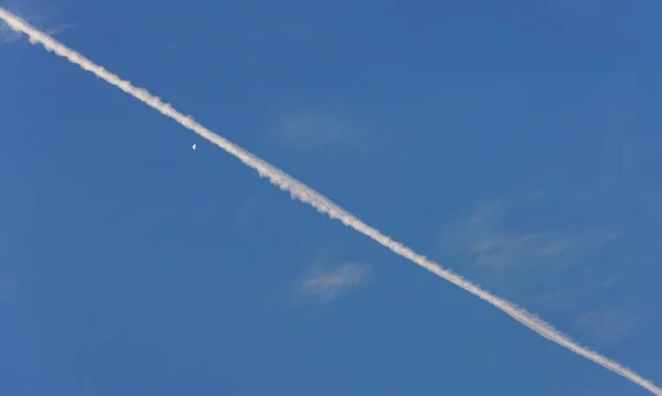 飛行機の白いピンクの結露歩道 陰謀説でケムトレイルとしても知られている を斜めに澄んだ朝の空 月の近くに描かれた — ストック写真