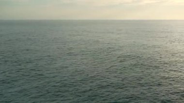 Güneş denizin üstünde yükseliyor, kıyılar kayalık.