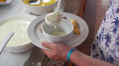Genç adam porselen kaseye krema koyuyor, açık büfede pasta taşıyor.