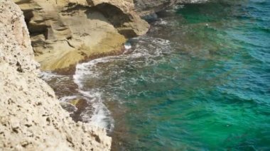 Güneşli bir günde kayalık kıyıya çarpan küçük dalgalar yukarıdan yavaş çekim videolarına bakıyor.