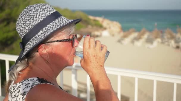 Starsza Kobieta Kapeluszu Plażowym Pijąca Szkła Szukająca Rozmazanego Tła Plaży — Wideo stockowe