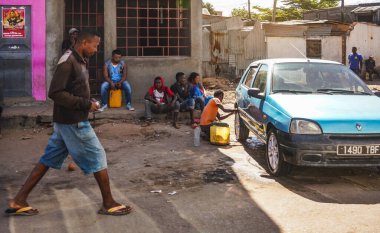Ilakaka, Madagaskar - 05 Mayıs 2019: Taş verandada oturan bir grup meçhul insan, araba tekerleklerini temizleyen bir adam, önlerinde yürüyen başka bir kişi, yoksul evler ve kulübeler
