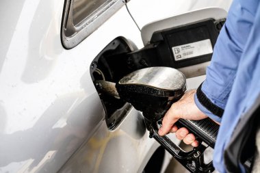 Yakıt hortumunu tutan, benzin deposunu dolduran, yağmur damlalarıyla kaplı bir adam.