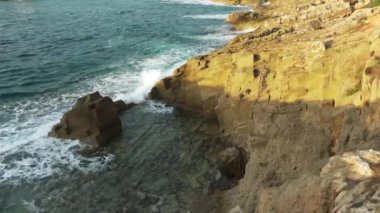 Güneşli bir günde kayalık kıyıya vuran küçük dalgalar yukarıdan bize bakıyor.
