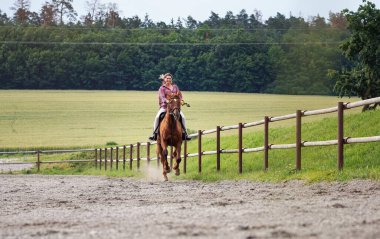 Kum çitlerinin orada kahverengi ata binen genç bir kadın, hızlı hareket eden saçlar