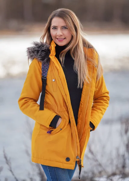 暖かいオレンジ色の黄色の冬のジャッキで若い女性のカジュアル肖像画 ジッパーダウン ぼやけた背景彼女の後ろ — ストック写真