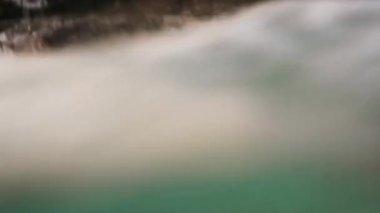 Sualtı videosu. Kumsalın yanında kirli deniz suyu, kumların üzerinde hareket eden kuru algler, kahverengi kayalıklar.