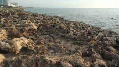 Kayalık sahil uçurumundan denize doğru yürüyorum, uzaktaki turistik otellere gidiyorum.