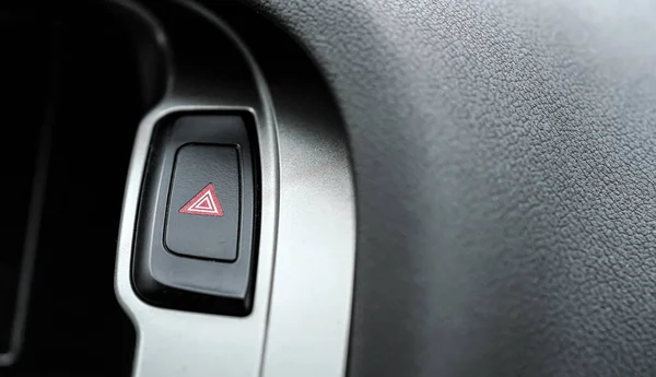 Red warning light triangle button in modern car interior panel, closeup detail