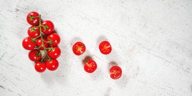 Vibrant small red tomatoes with green vines on white stone like board, view from above, empty space for text right side.