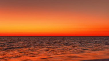 Vibrant orange red sky reflecting in calm ocean after sunset. Minimal landscape photo with space for text.