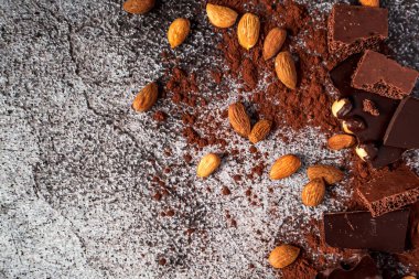 Çeşitli çikolata parçaları. Koyu acı ve süt gözenekli, kakao tozu, badem, fındık ve gri, tarafsız, beton bir arka plan..