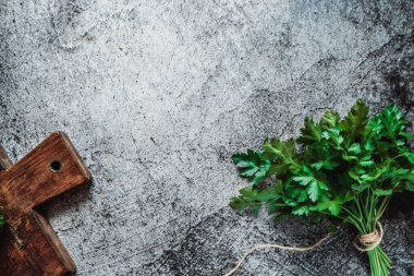 Yeşil kokulu maydanoz gri bir arka planda, tahta bir tahtanın üzerinde yatıyor. Mesaj için yer. Üst görünüm