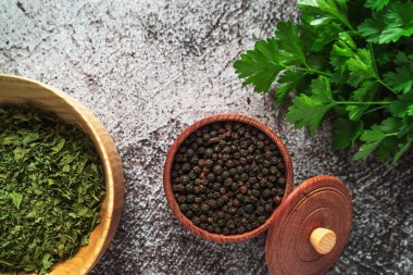 dry aromatic spices, black pepper in a wooden bowl, fresh green parsley on a gray concrete table