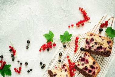 Dilimlenmiş ev yapımı böğürtlenli turta beyaz bir tahta üzerinde gri beton arka planda siyah ve kırmızı üzümlü üzümlü.