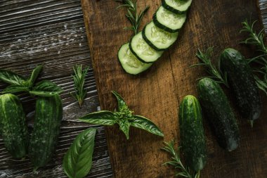 Fesleğenli ve biberiyeli yenebilir yeşil çiftlik salatalıkları. Kahverengi ahşap bir tahtanın üzerindeki sebzelerin dokusu.