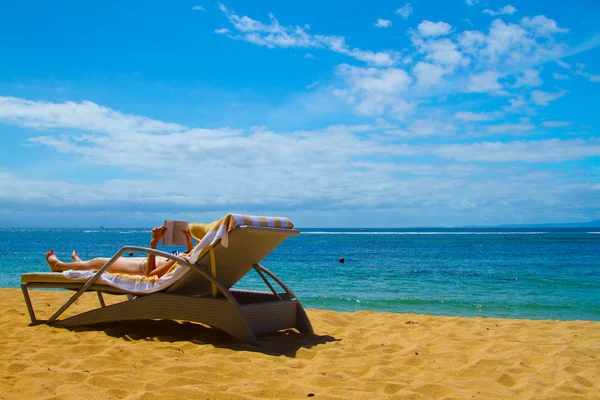 Young girl with hiding face under a hat reads a book lying on a plank bed on a beach. Royalty Free Stock Images