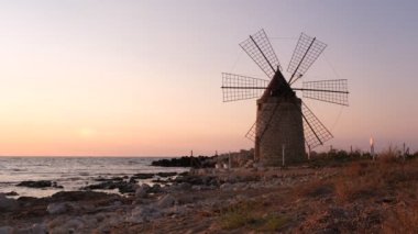 Windmill on the shore seaside with sunset in the background. North of Sicily, Trapani, old fashioned windmill on the coast
