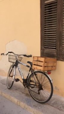 Vintage old bicycle with basket and wooden basket at the back on the typical Italian alley against yellow rustic wall
