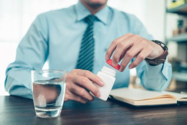 İş adamı masanın üstünde şişe hapı ve su bardağı açıyor..