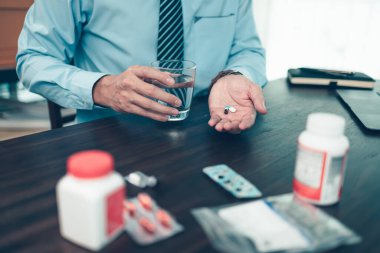 Bir bardak suyla çalışan bir işadamı elinde haplar tutuyor. Çalışma ve hastalıklı konsept.