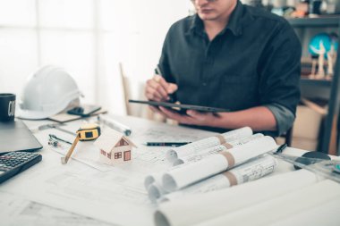 Mini model ev, tablet arka planı üzerinde çalışırken plan üzerinde çalışıyor. Ev Mimarı tasarımı ve mühendisi konsepti.