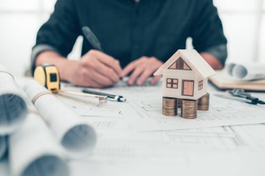 Mini model ev. Tasarımın üzerinde para madeni para var. Mezura, pusula, kalem ve kaskı masaya koyun. Maliyet Mimarı ve Mühendislik kavramı.