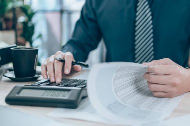 Şirket verilerini, belgelerini ve raporlarını masa başında hesaplamak için hesap makinesi üzerinde çalışan bir muhasebeci. Muhasebe iş konsepti.