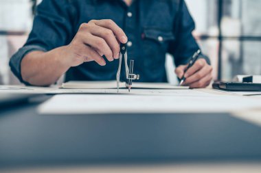 Bölücü pusula kullanan mimar plan üzerinde çalışıyor ve deftere not alıyor. İnşaat konsepti. Mühendislik araçları