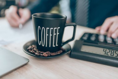 Ofis masasında bir fincan kahve ve hesap makinesi üzerinde çalışan muhasebeci şirket verilerini, belgelerini ve raporlarını masabaşında hesaplıyor. Muhasebe iş konsepti.